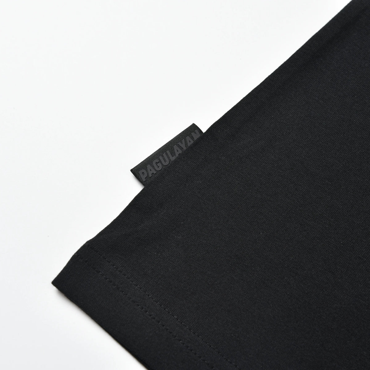 Close-up of the Pagulayan logo tag near the waist of the black Stripe Pagulayan Logo Shirt.