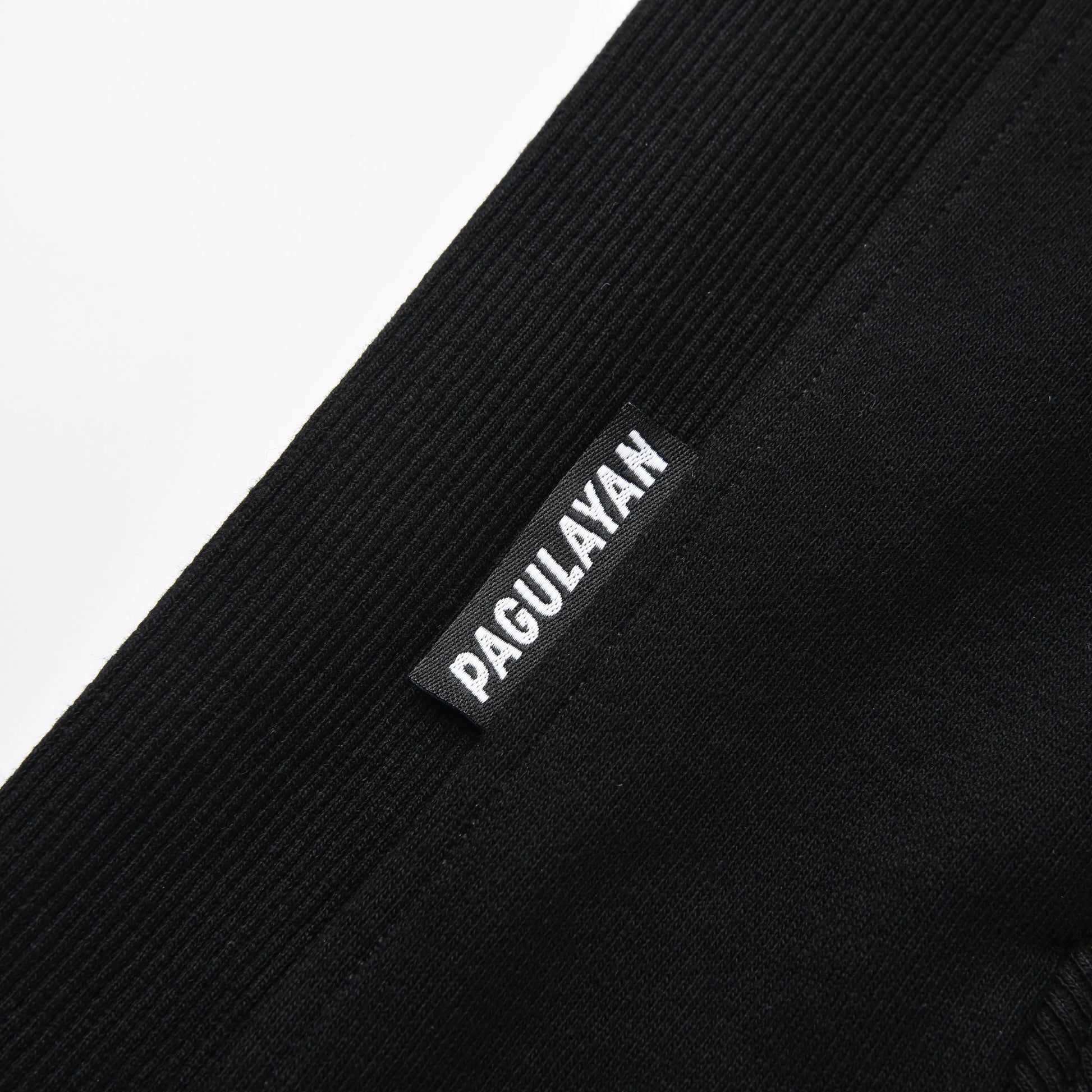 Close-up of the Blackout Hoodie hem showing the woven Pagulayan brand label on the ribbed fabric.