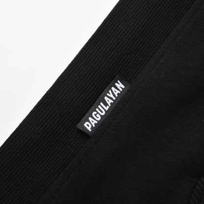 Close-up of the Blackout Hoodie hem showing the woven Pagulayan brand label on the ribbed fabric.