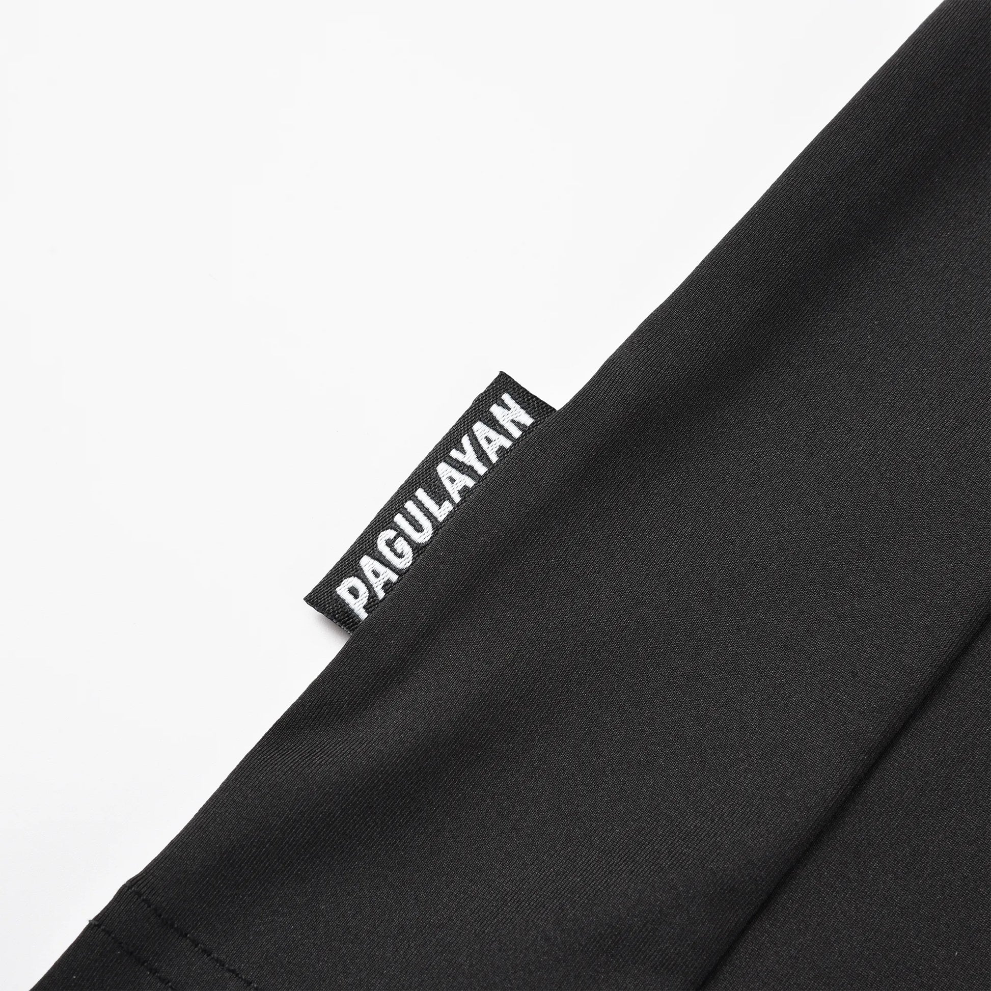 Close-up of the Pagulayan brand tag stitched on the hem of the black Pagulayan Jersey.
