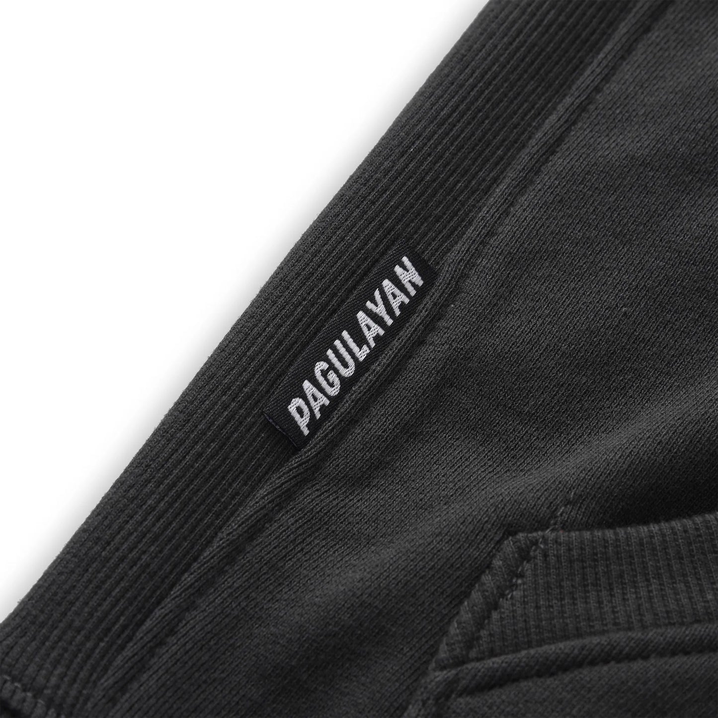 Close up of the Pagulayan Men’s Pocket Hoodie hem showing the woven brand label and ribbed fabric texture.