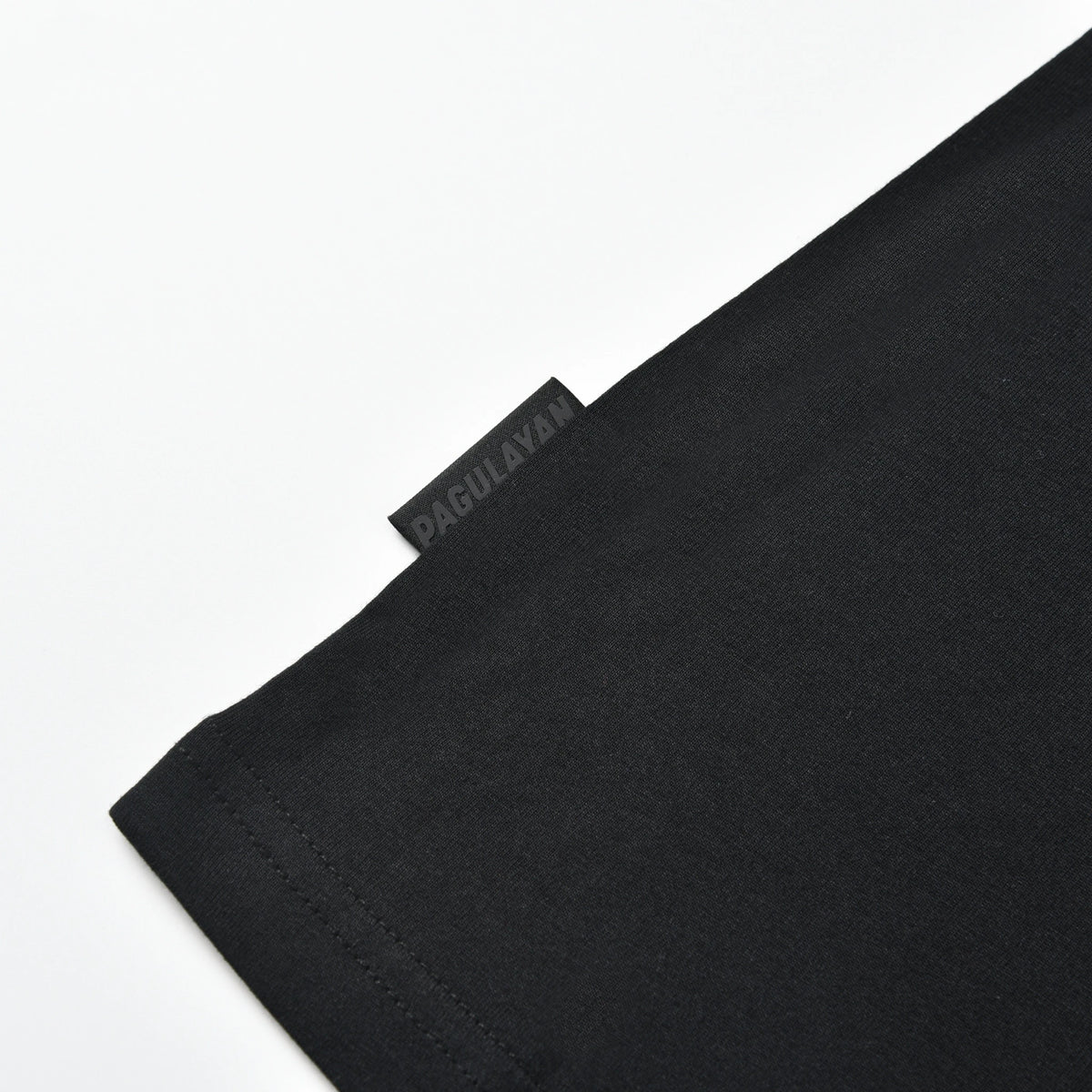 Close-up of the Pagulayan side tag and hem detail on the black PAGS Shirt.