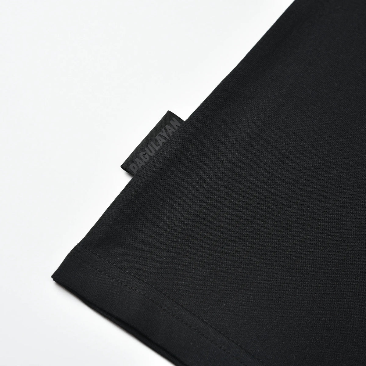 Close-up of the Pagulayan side tag and hem stitching on the black Small Pagulayan Logo Shirt.