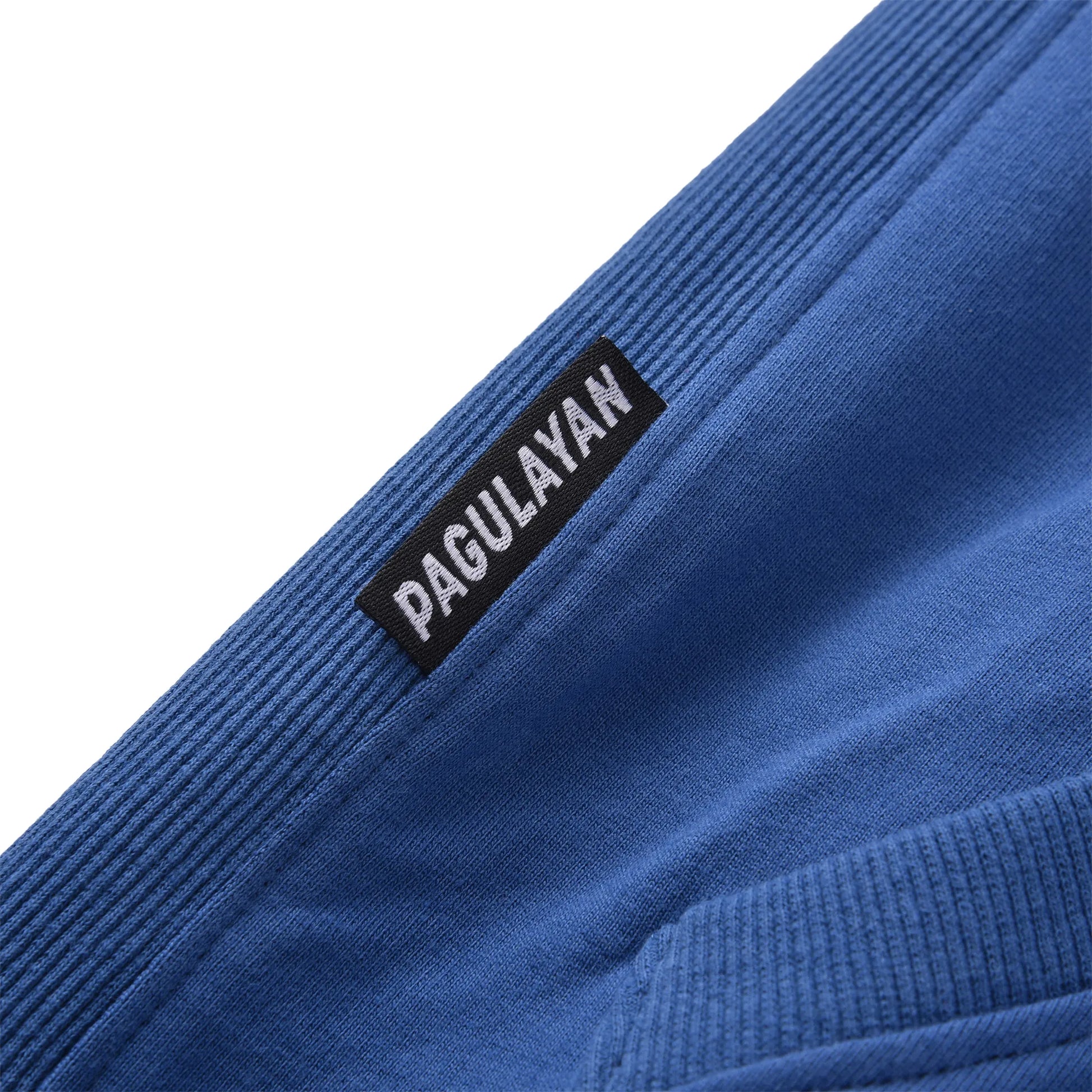 Close up of the Pagulayan Women’s Drop-Shoulder Pocket Hoodie hem label showing the woven brand tag and ribbed fabric.